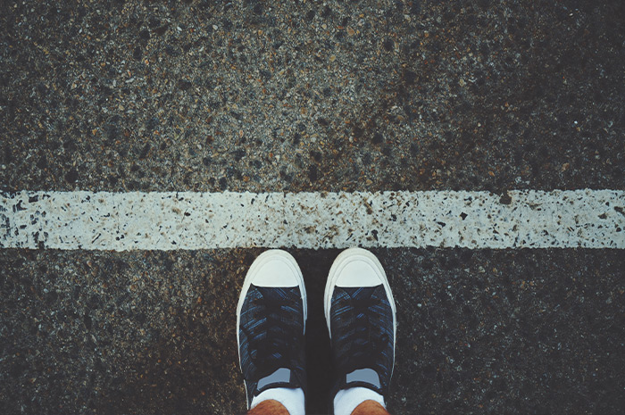 Ein Bild, das Füße in Turnschuhen zeigt, die vor einer auf den Boden gemalten weißen Linie stehen.