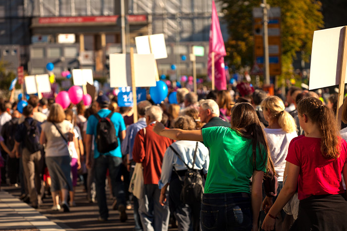 Ein Bild, das eine bunte Menschenmenge mit Schildern und Ballons bei einer Demonstration zeigt.